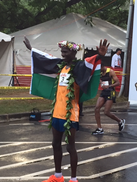 Champion's pose as fifth-place finisher and pre-race co-favorite Yemane Adhane of Ethiopia suffers in the background.